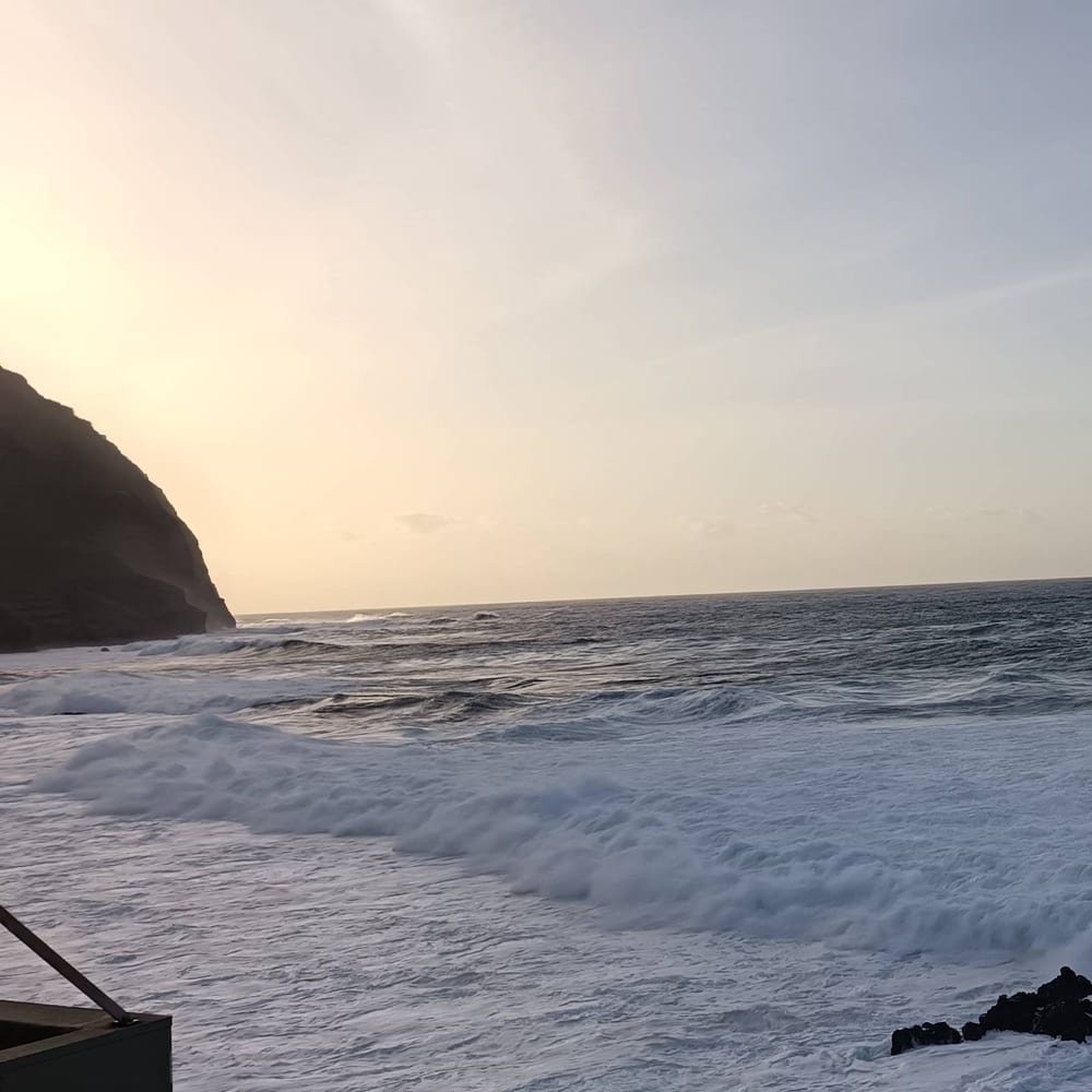 A wave crashing at golden hour beside a Madeira cliff silhouette